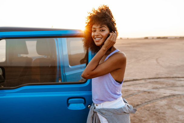 Photo of an african american woman standing at her car on beach at sunrise - Valokuva, kuva