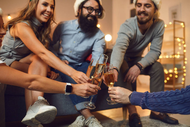 Group of young happy friends sitting and drinking champagne during Christmas holiday festive party - Foto, imagen