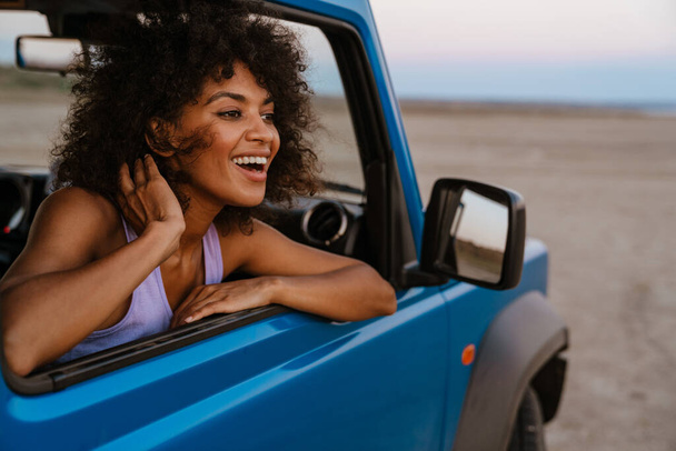Image of cheerful african american woman smiling while travelling in car on desert - Photo, Image