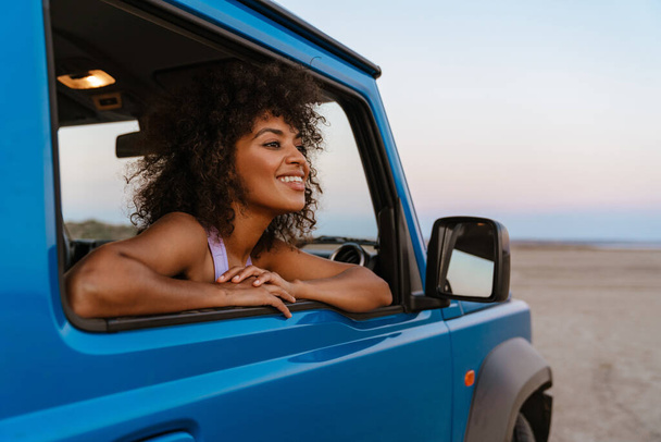 Obraz wesołej afrykańskiej kobiety uśmiechniętej podczas podróży samochodem po pustyni - Zdjęcie, obraz