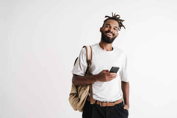 Photo of joyful african american guy smiling and using mobile phone isolated over white background - Valokuva, kuva