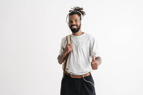 Photo of joyful african american guy using headphones while showing thumb up isolated over white wall - Fotoğraf, Görsel