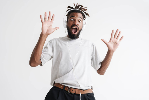 Photo of shocked african american guy in headphones expressing surprise isolated over white background - Фото, изображение