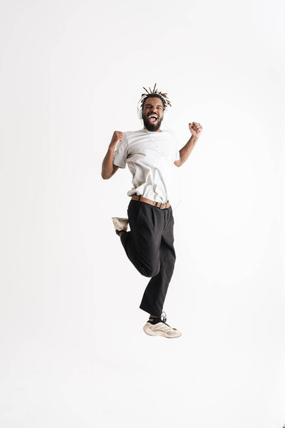Photo of excited african american guy in headphones laughing while dancing isolated over white background - Foto, Imagen