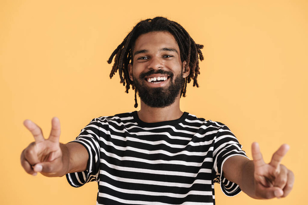 Photo of cheerful african american guy showing peace gesture isolated over yellow background - Foto, afbeelding