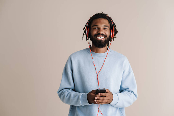 Cheerful african american guy in headphones using mobile phone isolated over white background - Фото, изображение