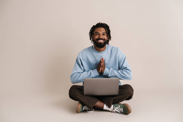 Happy african american guy sitting with laptop on floor isolated over white background - Φωτογραφία, εικόνα