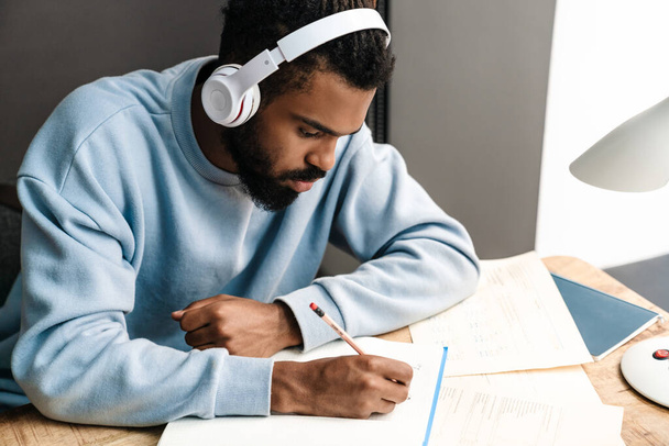 Confident young african man studying at the desk, wearing wireless headphones - Фото, изображение