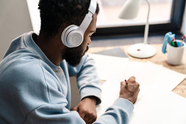 Top view of a confident young african man studying at the desk, wearing wireless headphones - Photo, Image
