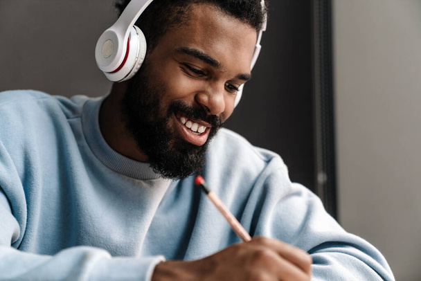 Confident young african man studying at the desk, wearing wireless headphones - Fotó, kép