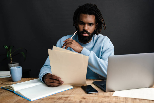 Komea vakava nuori afrikkalainen mies istuu kahvilassa mietteliäs ilme, ajatellut liiketoimintasuunnitelmia, työskentelee kannettavan tietokoneen - Valokuva, kuva
