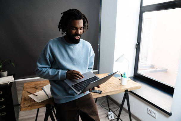 Confident afro american man working on laptop computer while leaning on a desk - Foto, Bild