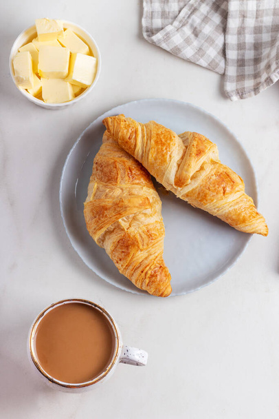 Fresh french croissants on plate, cup of coffee and milkman in the morning light. Continental morning breakfast on marble background. - 写真・画像