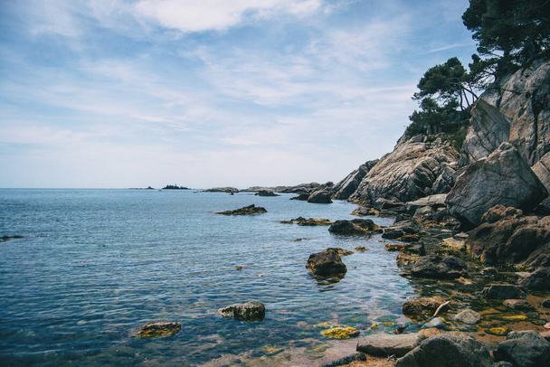 Paisagem de uma pequena praia de seixos cercada por rochas com vegetação na Costa Brava - Foto, Imagem