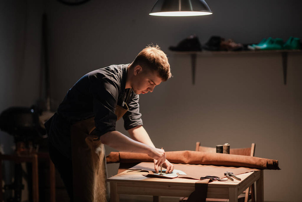 un joven maestro en la producción manual de zapatos en su taller está trabajando en la creación de zapatos. - Foto, Imagen