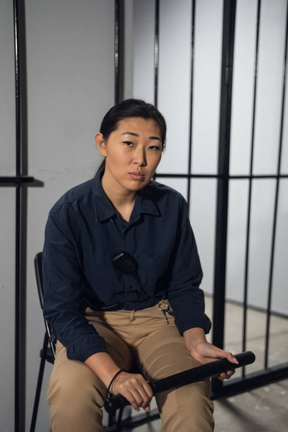 Asian female taskmaster sits in the background of cells with prisoners in a womens prison - Photo, Image