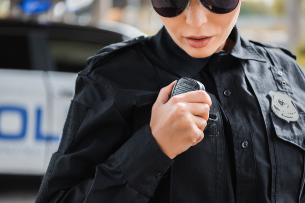cropped view of young policewoman talking on radio set on blurred background outdoors - Foto, imagen