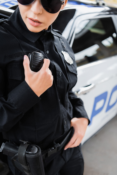 vista ritagliata di giovane poliziotta che parla alla radio impostato su sfondo sfocato all'aperto - Foto, immagini
