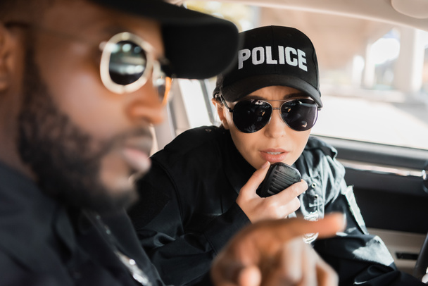 policía hablando por radio con un borroso colega afroamericano en primer plano en patrulla - Foto, Imagen