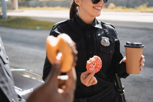 cropped view of policewoman with doughnut and paper cup on blurred foreground outdoors - 写真・画像