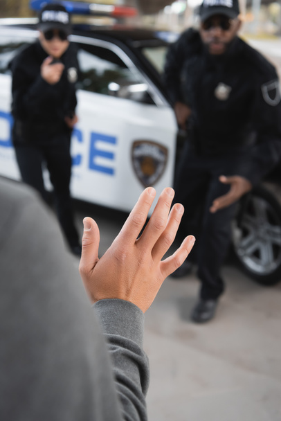 close up view of offender showing hand with blurred multicultural police officers on background outdoors - Photo, Image