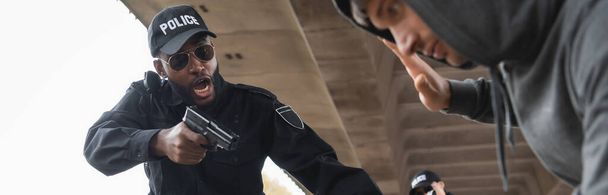 agresivní afroameričtí policisté křičí, zatímco míří pistolí na odevzdané pachatele na rozmazané popředí - Fotografie, Obrázek