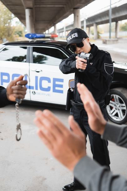 前景にアフリカ系アメリカ人の同僚をぼやけたまま屋外に投降した犯人を狙う警察官 - 写真・画像