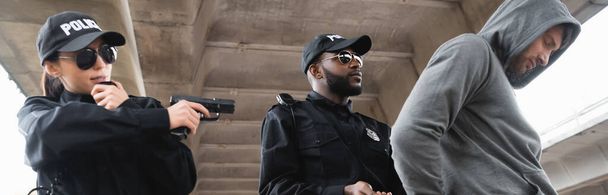 афроамериканський поліцейський заарештовує з капюшоном злочинця поблизу колеги, прицілюючись пістолетом на відкритому повітрі, банер
 - Фото, зображення