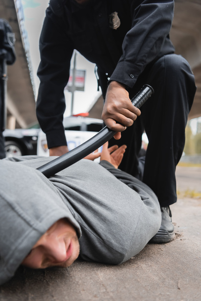 african american policeman with truncheon arresting hooded offender lying on street on blurred background - Fotoğraf, Görsel