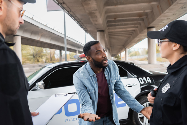 irritado afro-americano vítima gestos enquanto discutindo com policiais em fundo turvo na rua urbana - Foto, Imagem