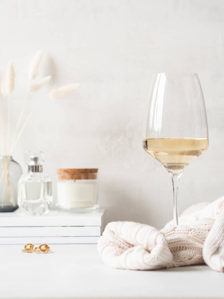 Modernes, feminines Stillleben aus Glas Weißwein, Pullover und verschiedenen Gegenständen auf dem Schminktisch. Frontansicht. Kopierraum - Foto, Bild