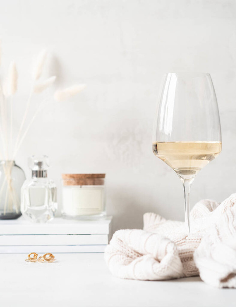 Modern feminine still life of glass of white wine, sweater and various items on the dressing table. Front view. Copy space - 写真・画像