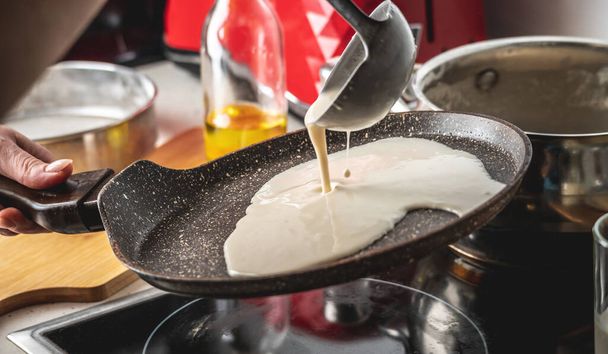 Iemand giet het deeg in een hete pan en bakt heerlijke zelfgemaakte pannenkoeken. Concept van pannenkoeken bakken in je eigen keuken. - Foto, afbeelding