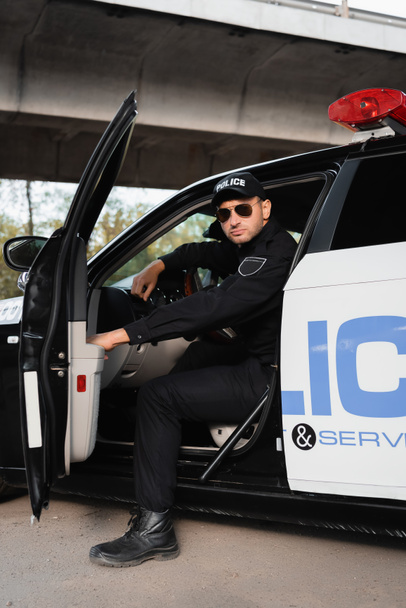 Güneş gözlüklü bir polis, şehirde arabada oturuyor.  - Fotoğraf, Görsel