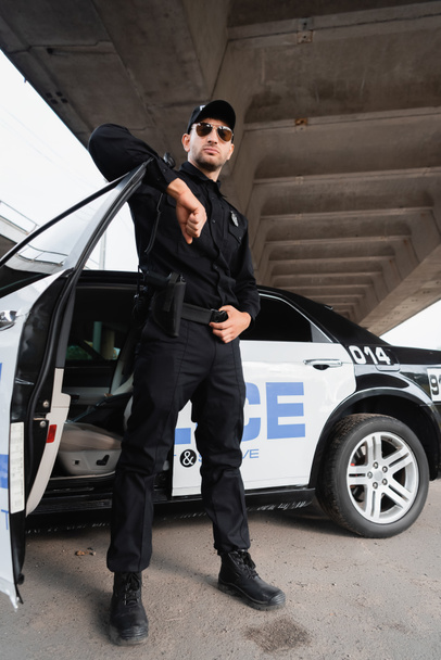 Officer of police in sunglasses and uniform standing near car on urban street  - Fotoğraf, Görsel