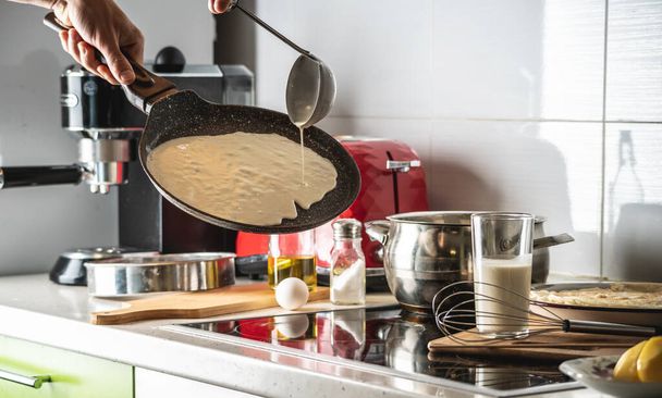 Egy ember, aki a tésztát forró serpenyőbe önti, és finom házi palacsintát süt. A palacsinta készítésének koncepciója a saját konyhádban. - Fotó, kép
