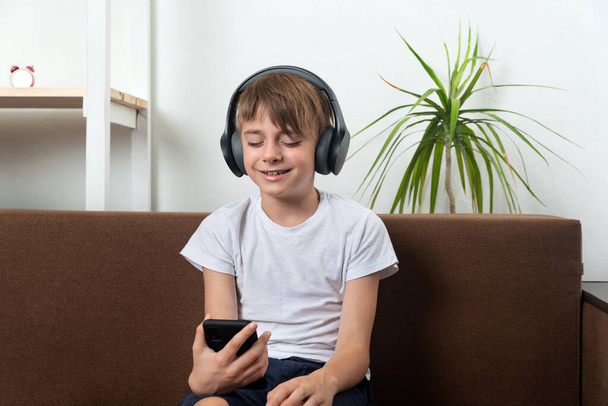 Chłopiec ze słuchawkami i telefonem w rękach słucha muzyki i śpiewa. - Zdjęcie, obraz