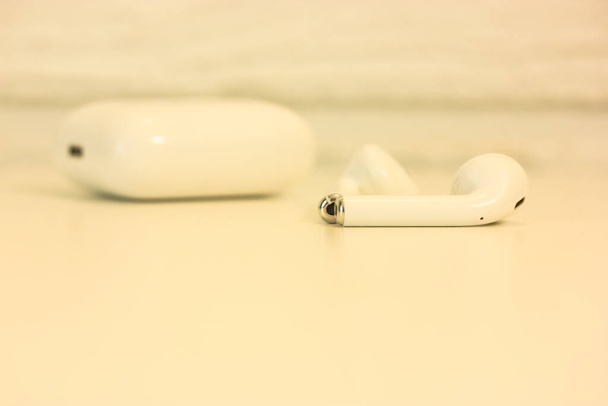 Weiße Airpods-Kopfhörer auf einem weißen Tisch, ein Gerät zum Musikhören - Foto, Bild