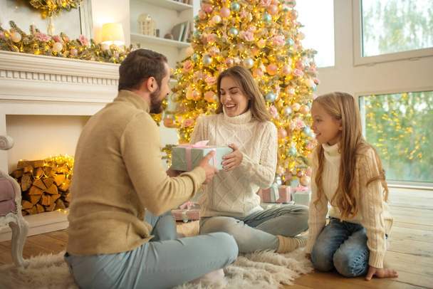 Young family sitting on the floor and exchanging christmas gifts - Foto, Imagen