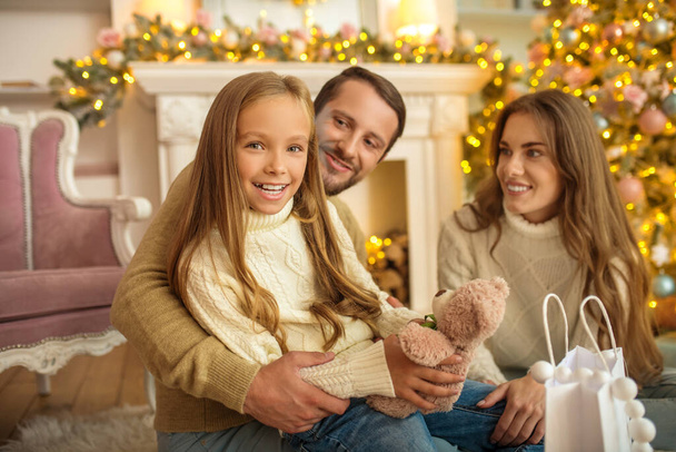 Young parents giving christmas gift to their daughter and family looking happy - Фото, изображение