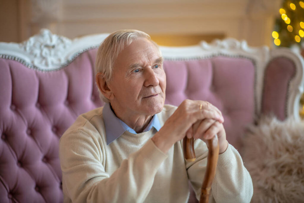 Grey-haired elderly man sitting on the sofa and looking aside - Photo, image