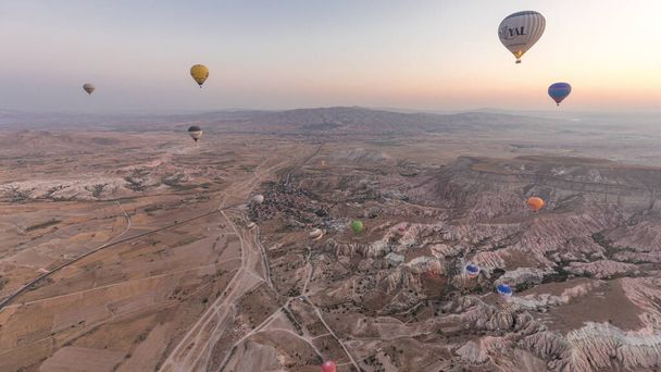 Aerial view from hot air balloon timelapse hyperlapse with other flying balloons during Sunrise over the fairytale landscape hills of Kapadokya. Goreme, Cappadocia, Turkey - Fotó, kép