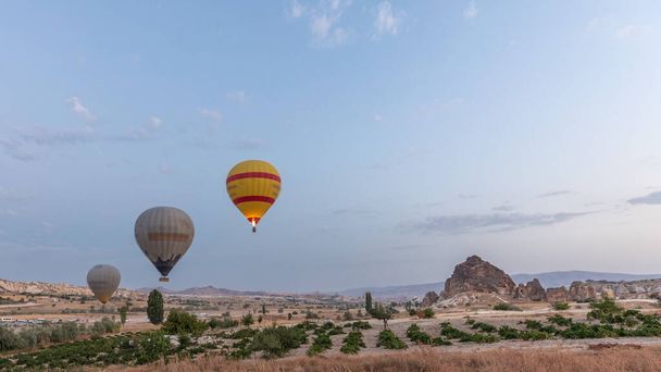 Beautiful colorful hot air balloons take off and flying in clear morning sky above unusual rocky landscape timelapse in Cappadocia, Turkey - Fotó, kép