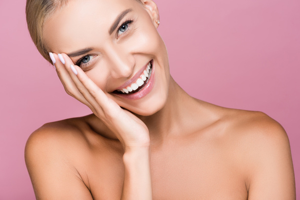 smiling beautiful blonde woman touching face isolated on pink - Photo, Image