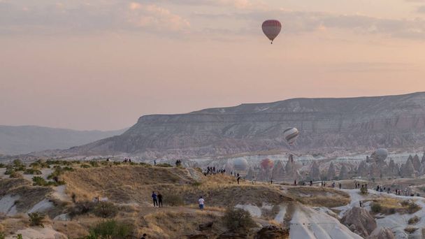 People watching a beautiful sunrise from viewpoint with colorful hot air balloons flying in clear morning sky above unusual rocky landscape aerial timelapse in Cappadocia, Turkey - Foto, Imagem