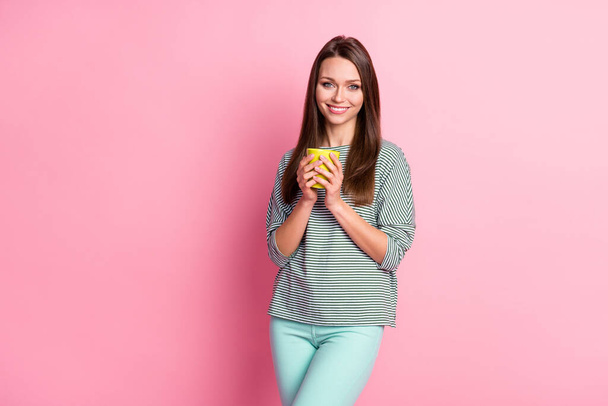 Photo of nice adorable brown long hair girl hold cup wear casual t-shirt pants isolated on pastel pink color background - 写真・画像