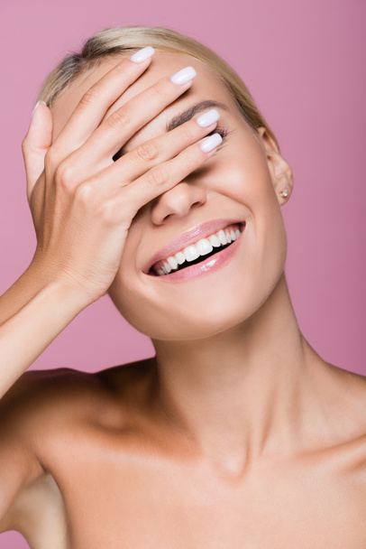 smiling beautiful blonde woman posing with hand on face isolated on pink - 写真・画像