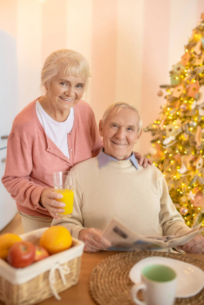Idős férfi ül az asztalnál, miközben a felesége narancslevet ad neki. - Fotó, kép