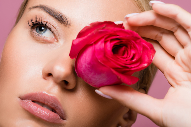 όμορφη ξανθιά γυναίκα με τριαντάφυλλο λουλούδι στο μάτι απομονώνονται σε ροζ - Φωτογραφία, εικόνα
