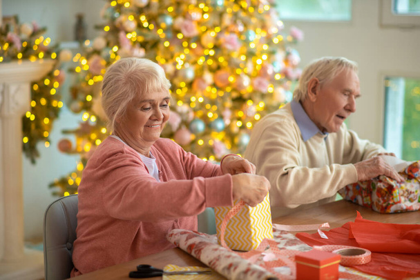 Elderly couple packing christmas gifts and feeling enjoyed - Fotó, kép